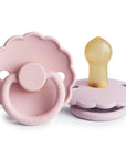 Two Frigg Daisy pacifiers in Baby Pink and Soft Lilac on a white background