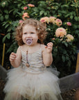 A little girl in a sparkly dress with a Soft Lilac Frigg Daisy pacifier, standing in a garden with flowers.