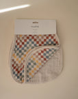 The mushie Organic Cotton Muslin Burp Cloth 2-Pack features colorful checkered cloths, partially folded to show the plain underside, displayed on a light beige surface with a shadow in the corner.