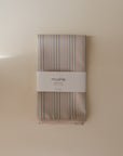 A folded, striped water-resistant Mushie Splat Mat with a pastel color palette, wrapped in a white label reading “Mushie Splat Mat,” displayed against a neutral background.