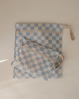 The mushie Water Resistant Wet Bag set includes two checkered pouches—one large with a wrist strap and one small—featuring blue and white squares, beige zippers, and ideal for diaper bag storage.
