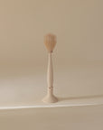 The mushie Silicone Baby Bottle Brush in beige features soft silicone bristles and a round head, stands upright in a matching holder, and is ideal for cleaning bottles and nipples against a neutral background.