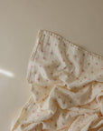 The mushie Organic Cotton Muslin Swaddle Blanket features soft, crumpled organic cotton with a subtle brown twig pattern on beige—perfect for swaddling or use as a cozy baby blanket.