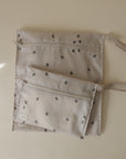 Two light beige mushie Water Resistant Wet Bags with small black and white floral prints and fabric loop handles are laid flat on a matching background. The larger bag sits behind the smaller, perfect for diaper bag storage.