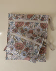 Two zippered fabric pouches with beige ribbons and a pastel daisy and poppy pattern make charming mushie Water Resistant Wet Bags—perfect for storing essentials or using in a diaper bag.
