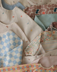 The mushie Long Sleeve Bib collection features water-resistant bibs with neat designs in pastel florals, stripes, checks, rainbows, birds, and abstract shapes.