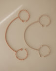 The mushie Adjustable Silicone Strap 2-Pack includes chic dusty rose and blush pink straps, each with a ridged chain linking two textured rings. Laid on beige, they're ideal as pacifier holders for your baby essentials.