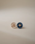 The FRIGG Little Viking Silicone 2-Pack by FRIGG—one beige and one dark blue pacifier—stands upright side by side on a softly lit, neutral-background surface.