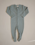 The mushie Zipper Pajama is a light blue, long-sleeve baby onesie with covered feet, laid flat on a plain surface. Featuring a front zipper from neckline to ankle, it's perfect for cozy and comfortable baby sleepwear.