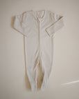 The mushie Zipper Pajama is a cream-colored, long-sleeve baby onesie with footed legs and a front zipper, made from cozy organic cotton. It is shown laid flat on a neutral background.