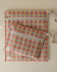 The mushie Water Resistant Wet Bag includes two zipper pouches with wrist straps, featuring a retro floral design in orange, blue, yellow, and pink on beige—ideal for diaper bag storage.