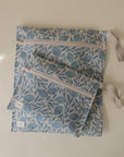 Two light blue mushie Water Resistant Wet Bags with floral designs and beige straps rest on a neutral surface. The larger bag is underneath the smaller, both featuring white tags on their seams.
