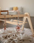 The mushie Chain Link Rings hang from a wooden baby gym over a soft pink blanket in a cozy living room, with a couch and coffee table in the background, encouraging your baby's fine motor skill development.