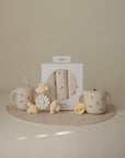 Neutral-toned baby products from mushie, including the Suction Spinner Toy, are arranged on a matching mat with delicate floral patterns against a beige background.