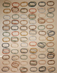 A grid of mushie Chain Link Rings—oval stroller toy links in muted colors—are evenly arranged on a light beige background with soft lighting, ideal for encouraging fine motor skills.