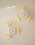 Four pastel yellow mushie Suction Spinner Toys shaped like turtles and two white daisy spinners are symmetrically arranged on a beige background, forming a playful, minimalist pattern that invites a fun sensory experience.
