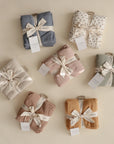Three organic cotton muslin cloths by mushie, neatly folded with a ribbon and white tag, come in various patterns—ideal for your nursery or diaper bag.