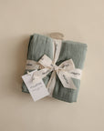 The mushie Organic Cotton Muslin Cloths 3-Pack, neatly folded and tied with a white ribbon and tag, is perfect for nursery or diaper bag essentials and displayed on a neutral beige background.