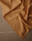 The mushie Organic Cotton Muslin Cloths 3-Pack features soft, light brown cloths with gentle folds and visible texture on a smooth beige surface—ideal for nursery needs.