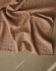 The mushie Organic Cotton Muslin Cloths 3-Pack features soft, light brown organic muslin on a neutral surface, highlighted by gentle natural light—ideal for nursery use or packing in your diaper bag.