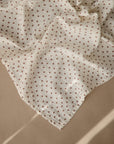 The mushie Organic Cotton Muslin Cloths 3-Pack, in cream with brown floral patterns, is shown draped on a beige surface with gentle sunlight—ideal for nurseries or as an essential in your diaper bag.