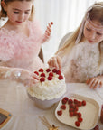 Two girls add raspberries to a cake on mushie Square Dinnerware Plates.