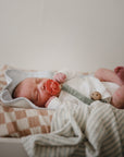 Newborn with pacifier, wrapped in blankets and wearing mushie Linen Pacifier Clip 2-Pack.