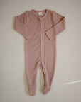 The mushie Zipper Pajama is a long-sleeved, footed baby sleepwear in soft dusty pink, laid flat on a light background. It features a front zipper from neck to leg for easy dressing and comfort.