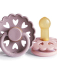 The FRIGG Andersen Fairytale Natural Rubber Pacifier 2-Pack by FRIGG features two pink pacifiers with scalloped edges and heart-shaped cutouts, including upright and flat positions showing the yellow natural rubber nipple and ring handle.