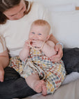 Woman holds smiling baby in romper with mushie No-Drop Sensory Teether.