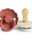 The FRIGG Daisy Natural Rubber Pacifier 2-Pack by FRIGG features two daisy-shaped pacifiers: one in dusty pink with a round handle and one in cream, both with scalloped edges and beige natural rubber latex nipples.