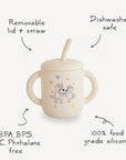 The Bluey x Mushie Silicone Training Cup + Straw by Mushie features two handles, a removable lid and straw, Bluey and Bingo designs, and is dishwasher safe. Made from 100% food-grade silicone—BPA/BPS/PVC/phthalate free for safety.