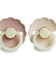 The FRIGG Daisy Night Natural Rubber Pacifier 2-Pack features two scalloped-edged pacifiers in pale pink and cream, each with a light green handle, round shield, and a natural rubber latex nipple for comfort.