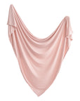 The mushie Stretchy Swaddle in soft light pink is draped in a wide, gentle curve with flowing folds and a triangular shape against a white background.