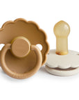 The FRIGG Daisy Natural Rubber Pacifier 2-Pack by FRIGG features two decorative flower-shaped pacifiers, including a tan daisy design with a scalloped edge and ring handle, and a white one, both with natural rubber latex nipples.