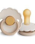 The FRIGG Daisy Natural Rubber Pacifier 2-Pack in Chamomile, a limited edition by FRIGG, features scalloped edges and round yellow handles, shown from front and side angles on a white background.