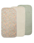 Three Mushie Changing Pad Liners are shown overlapping: one with a floral print, one in solid cream, and one in solid sage green. Each liner has rounded corners and a soft, quilted organic cotton texture.
