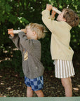 Two young children explore with mushie Kaleidoscopes surrounded by lush greenery.