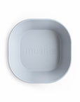 A BPA-free, square-shaped silicone dinnerware bowl by mushie in light gray, with rounded edges and "mushie" embossed at the center, shown on a white background.