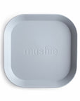 A square, light gray "mushie" Square Dinnerware Plate with rounded corners and the brand name embossed in the center, made from BPA-free plastic, is shown on a white background.