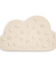 The mushie Cloud Teether is a beige, cloud-shaped silicone teether with embossed suns, moons, rainbows, umbrellas, and lightning bolts—crafted from safe silicone and marked with "mushie" at the bottom.