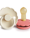 The FRIGG Daisy Natural Rubber Pacifier 2-Pack features scalloped-edge pacifiers—one beige showing the front and one pink displaying its natural rubber latex nipple and back. A beautiful, safe choice from FRIGG for parents.