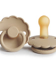 Two Croissant-colored FRIGG Daisy Natural Rubber Pacifiers (2-Pack) with scalloped edges, round handles, and the FRIGG brand at the base are shown—one from the front and one from the side. Limited Edition.