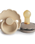 The FRIGG Daisy Natural Rubber Pacifier 2-Pack by FRIGG features two beige daisy-shaped pacifiers with scalloped edges, circular handles, and bulb-shaped natural rubber latex nipples shown from the front and side.