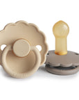 The FRIGG Daisy Natural Rubber Pacifier 2-Pack by FRIGG features two beige and taupe daisy-shaped pacifiers—one displayed front-facing with a ring, the other on its side showing the natural rubber latex nipple.