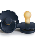 The FRIGG Daisy Natural Rubber Pacifier 2-Pack | Limited Edition features two dark blue pacifiers with scalloped edges—one shown face up and one on its side, highlighting the natural rubber nipple and textured handle.