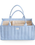 The mushie Diaper Caddy in Tradewinds is a light blue quilted tote with two handles and multiple beige interior compartments. A small white label is on the front. The organizer is empty and shown against a white background.