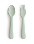 The mushie Dinnerware Fork and Spoon Set for children, in pale green non-toxic plastic, features the brand name embossed on each handle and is shown side by side on a white background.