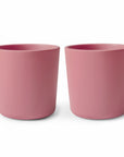 Two identical mushie Dinnerware Cups in matte pink are placed side by side on a white background. These kids' cups have a simple, cylindrical design with no handles or decorations.