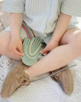 Child in stripes holds mushie Silicone Sensory Toy on blanket, playing to build fine motor skills.
